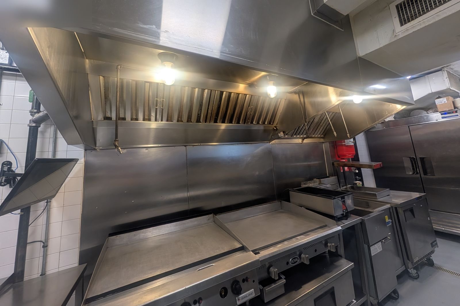 Clean commercial kitchen hood line with lights on above a cook line after professional cleaning